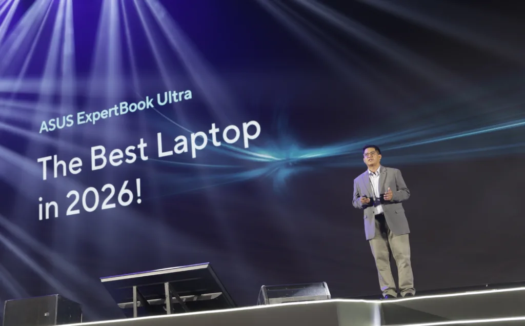 Speaker onstage in front of a screen reading The Best Laptop in 2026 with international tech review quotes praising the ASUS ExpertBook Ultra